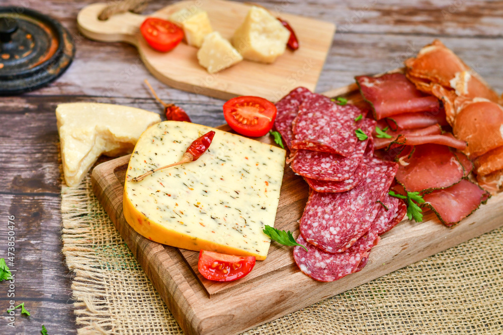 Italian dried thinly sliced artisan pork salami Milano , parmesan cheese, tomatoes and fresh basil on wooden background .Rustic home made italian snack. Italian dried thinly sliced artisan pork salami Milano , parmesan cheese, tomatoes and fresh basil on wooden background .Rustic home made italian snack.
