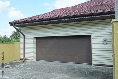 gray garage facade with brown gates under a tiled roof on the street on asphalt