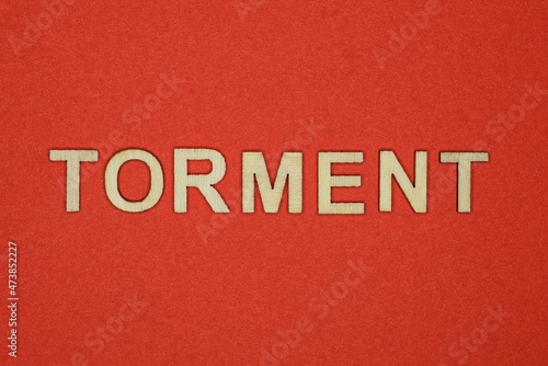 text the word torment from gray wooden small letters on an red table