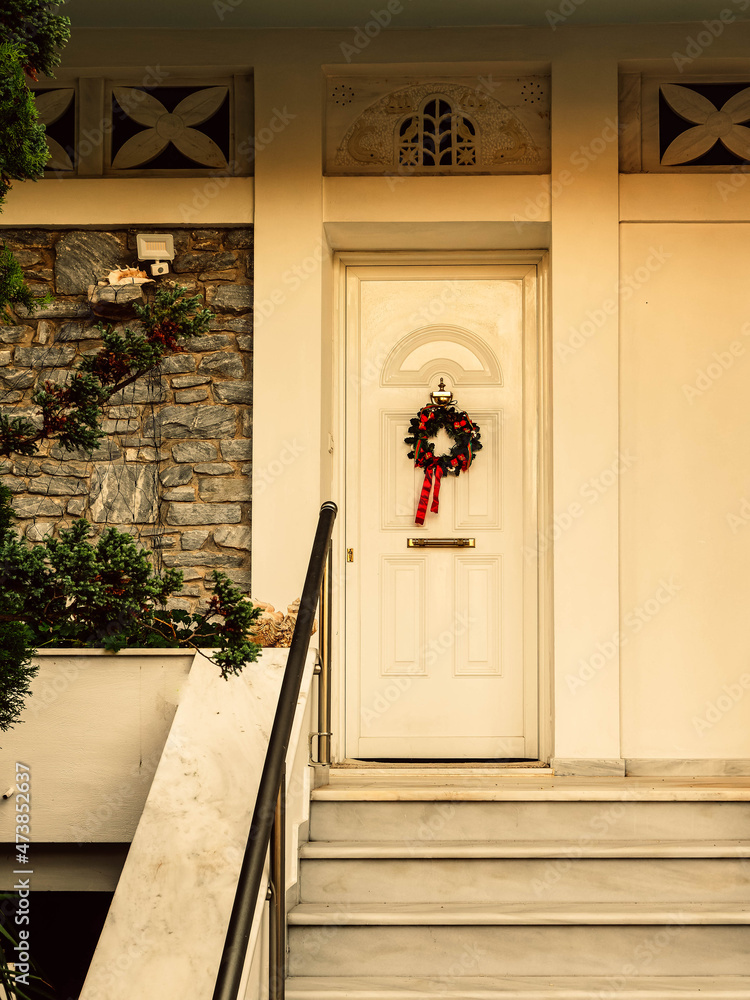 Fototapeta premium Christmas wreath decorated house entrance white door, with white marble stairs. Athens, Greece.