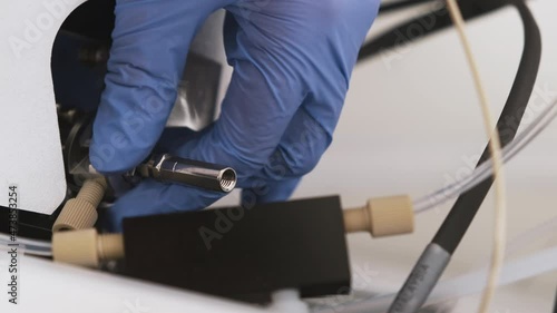 Laboratory worker inserts a nebulizer needle into ion source of mass detector. Maintenance or cleaning of LC MS qTOF . Liquid chromatography with mass detector for clinical or pharmaceutical analysis