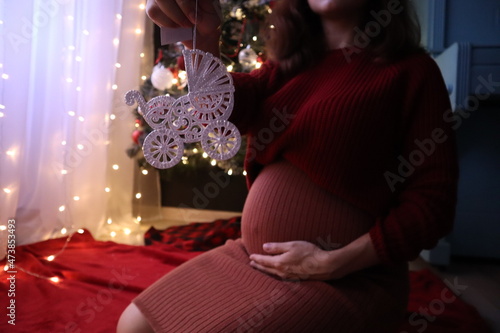 pregnant woman with toy stroller on the background of Christmas tree