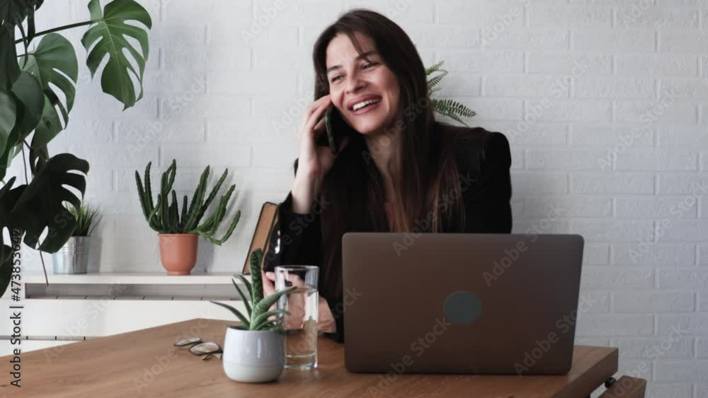 Smiling successful confident businesswoman talking on phone, sitting at desk with laptop, friendly manager consulting customer by phone, happy woman chatting with friends distracted from work Smiling successful confident businesswoman talking on phone, sitting at desk with laptop, friendly manager consulting customer by phone, happy woman chatting with friends distracted from work