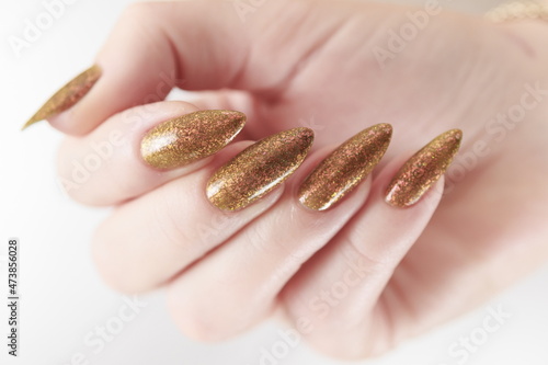 Female hand with long nails and a bottle of golden yellow mustard nail polish photo