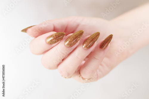 Female hand with long nails and a bottle of golden yellow mustard nail polish photo