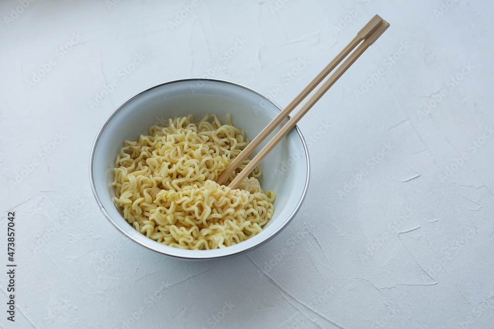 Instant noodles in a bowl with wooden chopsticks on a white textured background. Instant noodles in a bowl with wooden chopsticks on a white textured background.