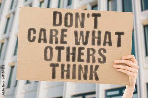 The phrase " Don't care what others think " on a banner in men's hand with blurred background. Psychology. Conflict. Behaviour. Human relationships. Success. Comment. Judge