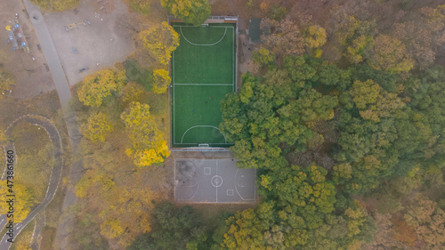 Football field with green grass and basketball court in city park in autumn. Leaf fall in the park. Aerial view.