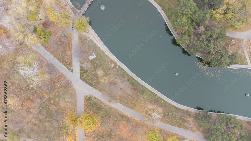 Walkways and footpaths in the city park in autumn. Leaf fall in the park. Autumn lake. Aerial view.