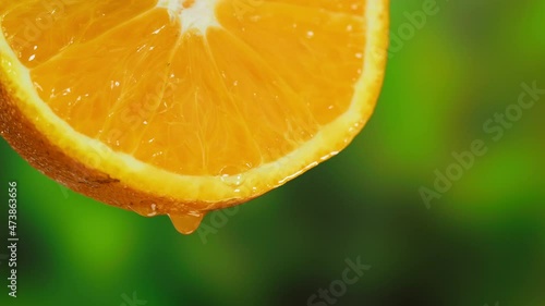 Drop falling from orange slice on nature background. Squeezing organic citrus juice close-up. Spa treatments. Skincare, cosmetics and beauty concept.
