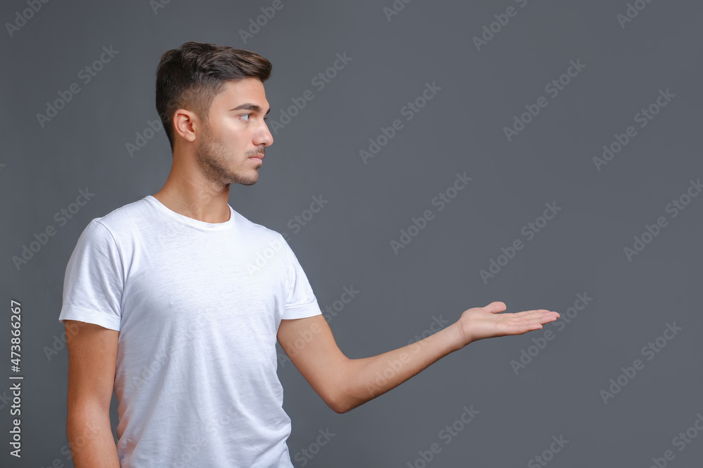 Young handsome man in a white t-shirt making gesture with hand isolated on a gray background. Copy space, profile view Young handsome man in a white t-shirt making gesture with hand isolated on a gray background. Copy space, profile view