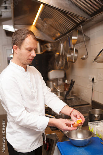 Vertical shot of a professional chef using eggs, preparing sauce at the kitchen