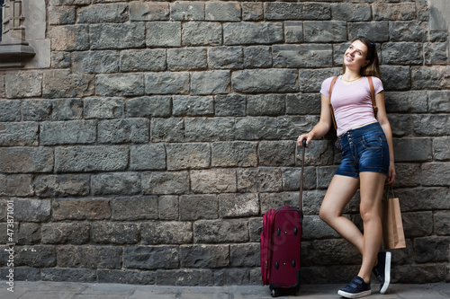 happy young woman with travelling bag on stone wall background outdoors
