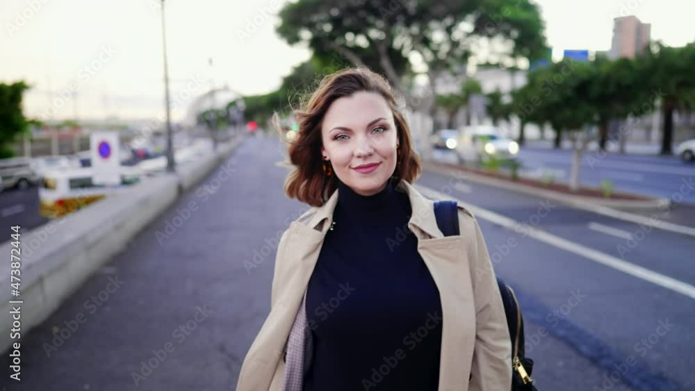Young pretty woman walks along busy city street with backpack on shoulder. Female student returns after classes from university. Lady tourist walking alone in Europe.