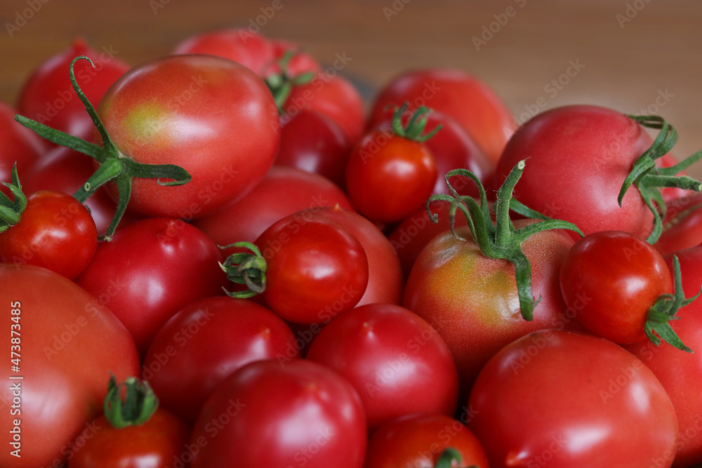 Background of beautiful and red tomatoes in basket. Tomato harvest. Top view. Fresh ripe organic juicy delicious tomatoes on wooden background. Healthy eating, vegetarianism, vegan