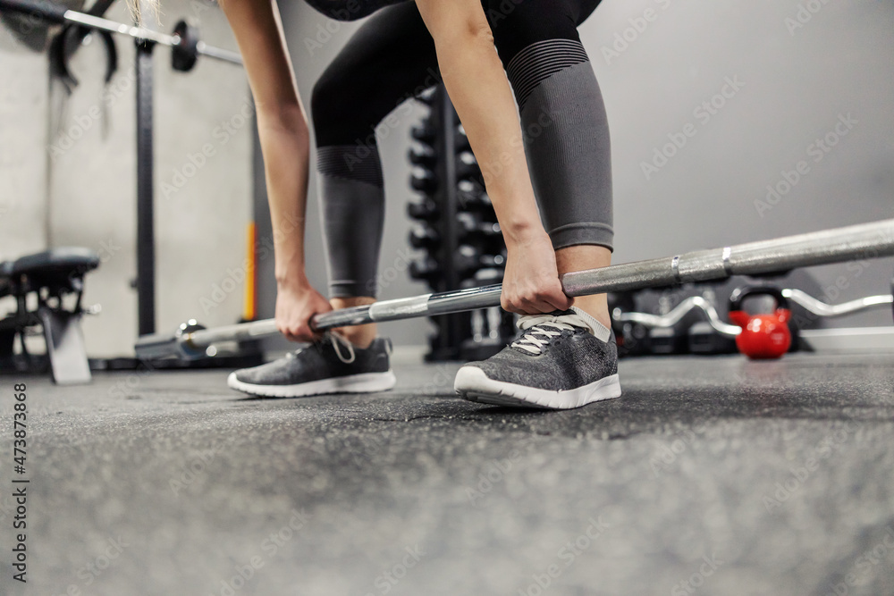 A portrait of a handsome body of a woman properly laid in a squat position without a face holding a barbell with both hands. Female hands hold the load and do a dead lift or squat A portrait of a handsome body of a woman properly laid in a squat position without a face holding a barbell with both hands. Female hands hold the load and do a dead lift or squat