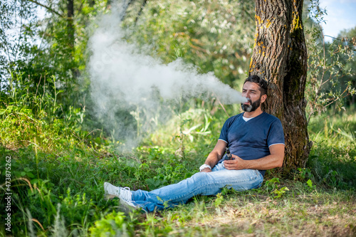 Stylish vape man blows up a couple an electronic cigarette in the forest. Handsome man. photo