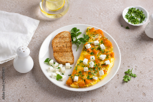 Obraz na płótnie Scrambled eggs omelet with pumpkin and feta on a white plate with toast and herbs on beige textured background