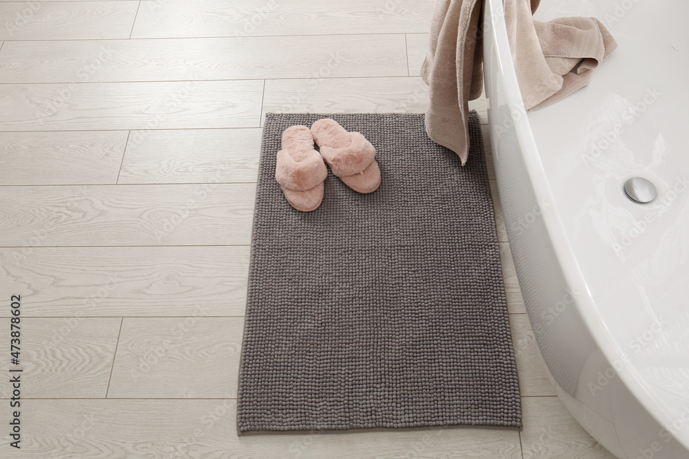 Soft grey bath mat and slippers on floor in bathroom - obrazy, fototapety, plakaty 