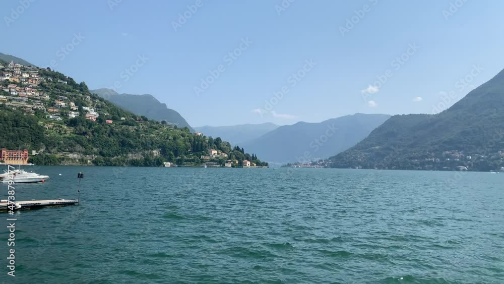 Panoramic motion view of Lago di Como lake. Mountainous lake shore with villages on the hills. View from Cernobbio town pier, harbour. Cernobbio, Lake Como, Lombardy, Italy. Panoramic motion view of Lago di Como lake. Mountainous lake shore with villages on the hills. View from Cernobbio town pier, harbour. Cernobbio, Lake Como, Lombardy, Italy.