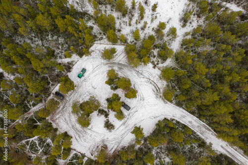 Aerial top down view on green camper van and parking lot. Beautiful forest in winter near Alta in Norway.