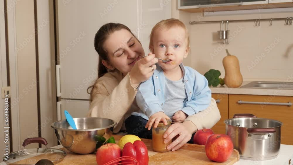 Little baby boy sitting on kitchen table and playing with utensils and cookware while eating from spoon. Concept of little chef, children cooking food, healthy nutrition Little baby boy sitting on kitchen table and playing with utensils and cookware while eating from spoon. Concept of little chef, children cooking food, healthy nutrition