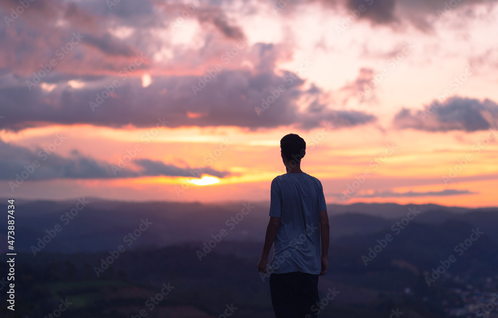 silhouette of a young man with the clouds and sunset in the background.