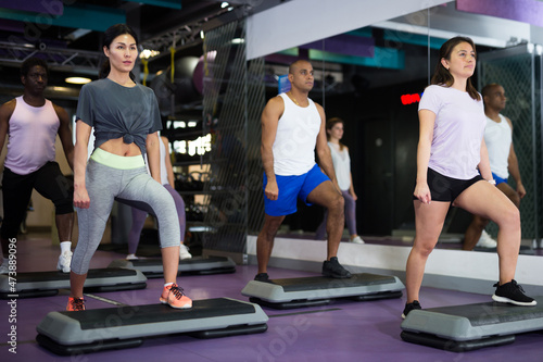 Sporty women and men doing cardio exercises training with step platforms at fitness center
