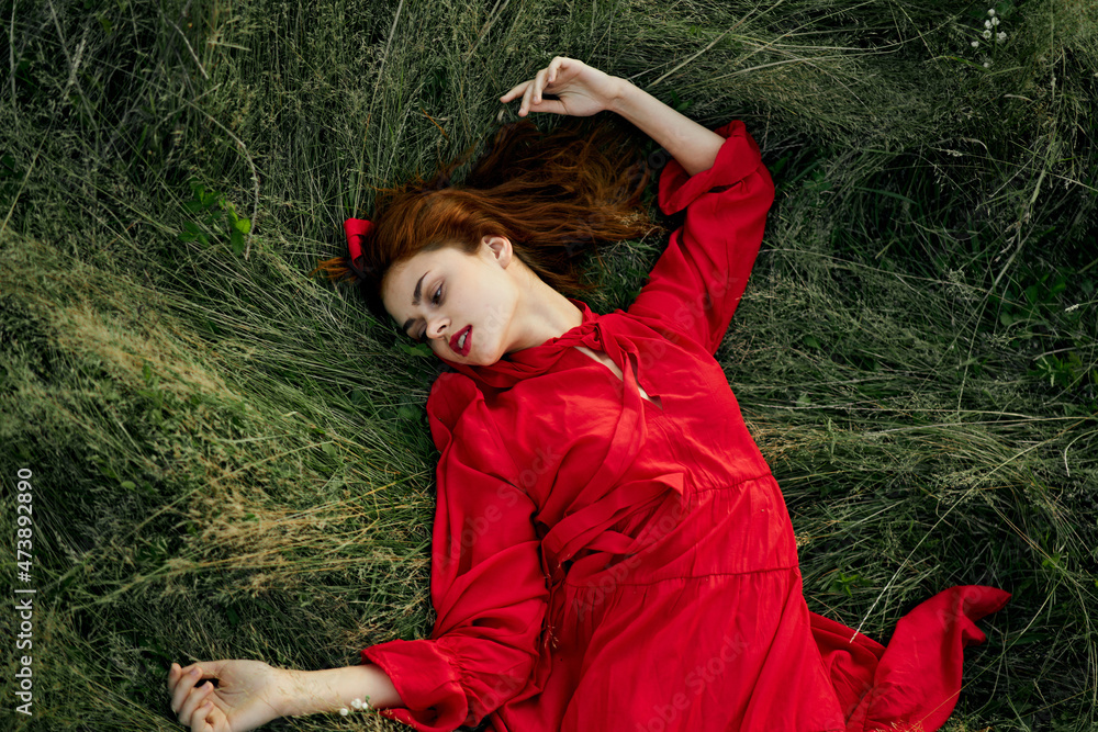 woman in red dress lies on the grass in the field nature landscape woman in red dress lies on the grass in the field nature landscape