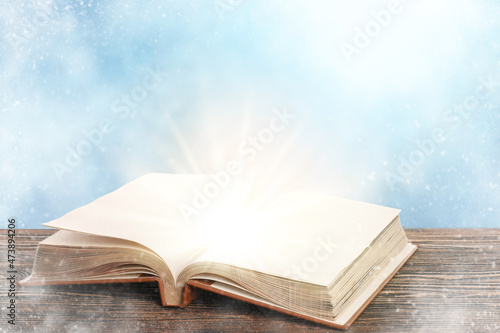 Open magic book on table against light background