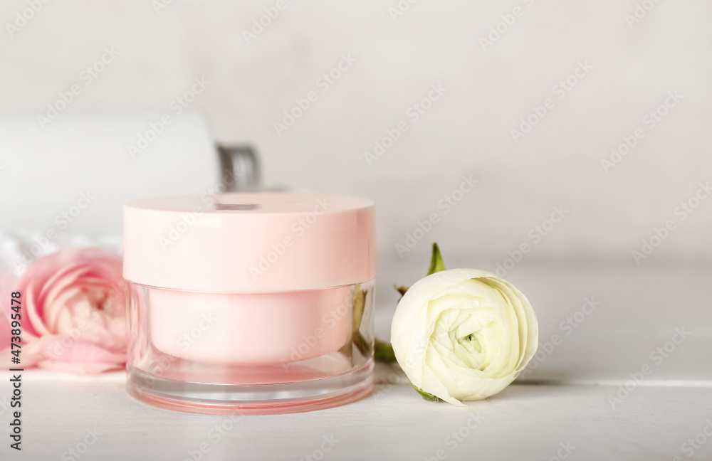 Jar of face cream and ranunculus flowers on wooden table Jar of face cream and ranunculus flowers on wooden table