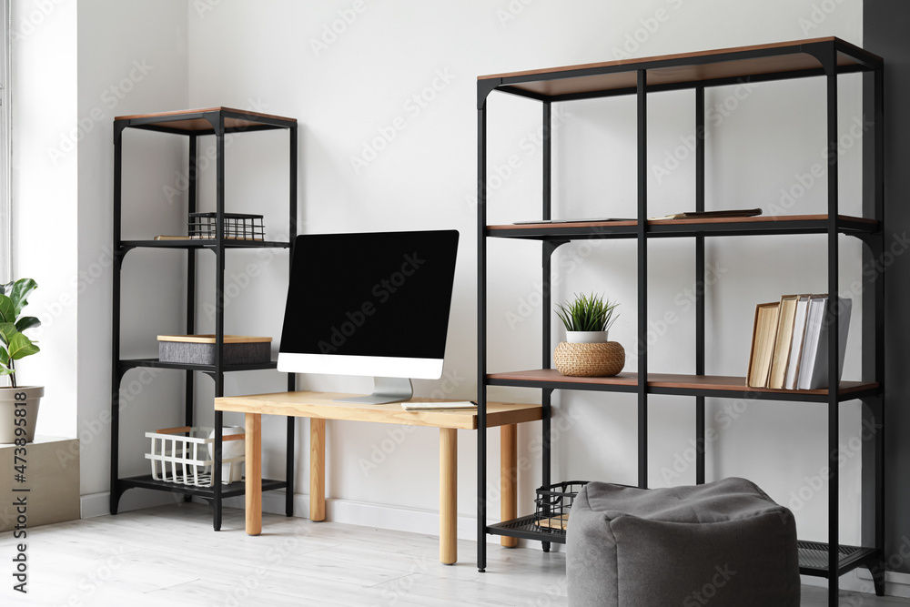 Interior of light room with table, computer screen and shelving units near light wall Interior of light room with table, computer screen and shelving units near light wall