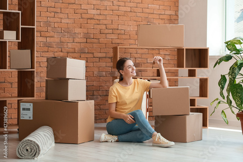 Happy young woman with key sitting on floor in her new apartment photo