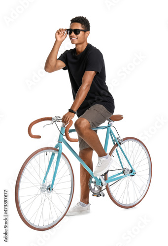 Fototapeta Naklejka Na Ścianę i Meble -  African-American teenage boy in sunglasses with bicycle on white background