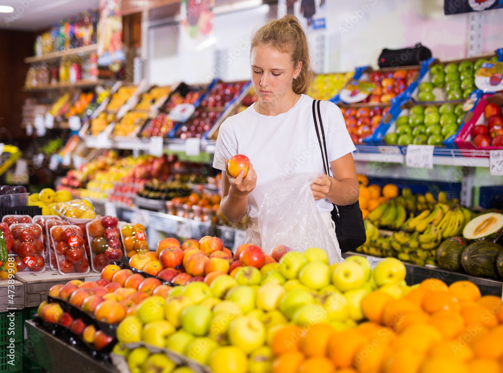 Young european woman purchaser choosing red organic apples in a grocery store