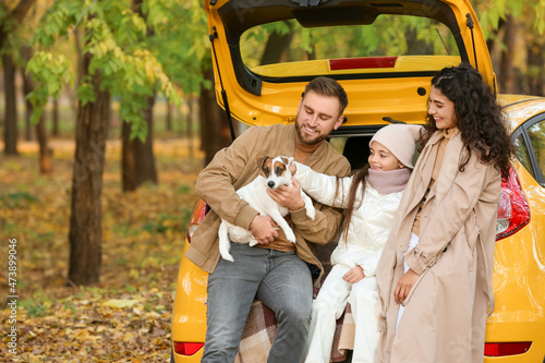 Happy parents with little daughter and cute dog sitting in car trunk on autumn day © Pixel-Shot