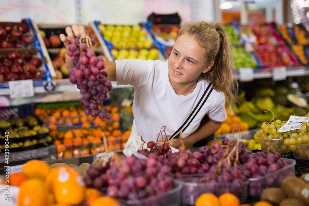 Young american girl choosing sweet grape at grocery section of supermarket