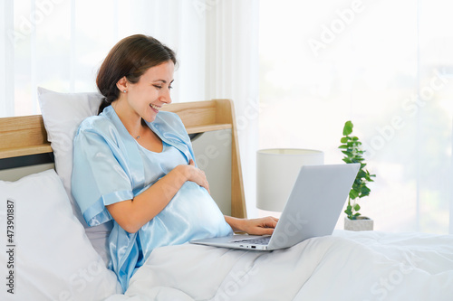 pregnant businesswoman sitting on bed at home working with laptop