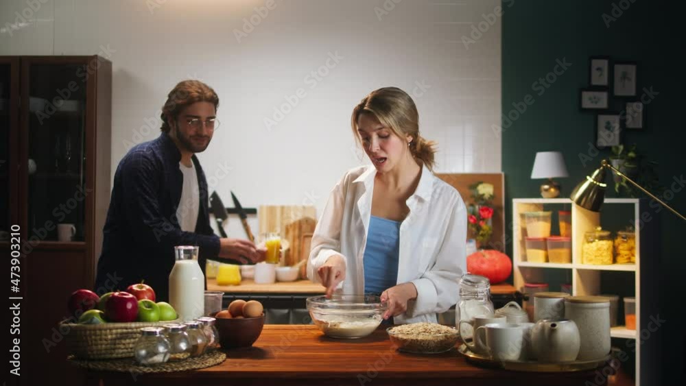 Loving couple, man and woman cooking family breakfast together in cozy kitchen. Young wife preparing ingredients, making dough mixture, while husband drinking orange juice. Romantic relationships. Loving couple, man and woman cooking family breakfast together in cozy kitchen. Young wife preparing ingredients, making dough mixture, while husband drinking orange juice. Romantic relationships.