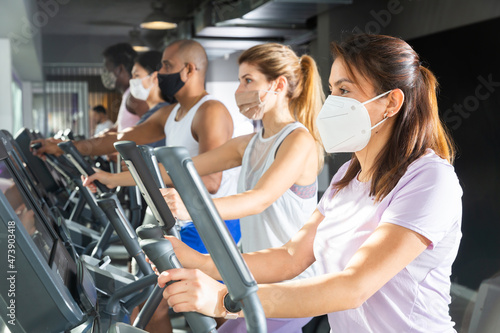 Portrait of sporty woman in protective face mask exercising on elliptical cross trainer in gym