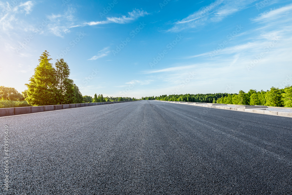 Straight asphalt road and green forest under blue sky Straight asphalt road and green forest under blue sky