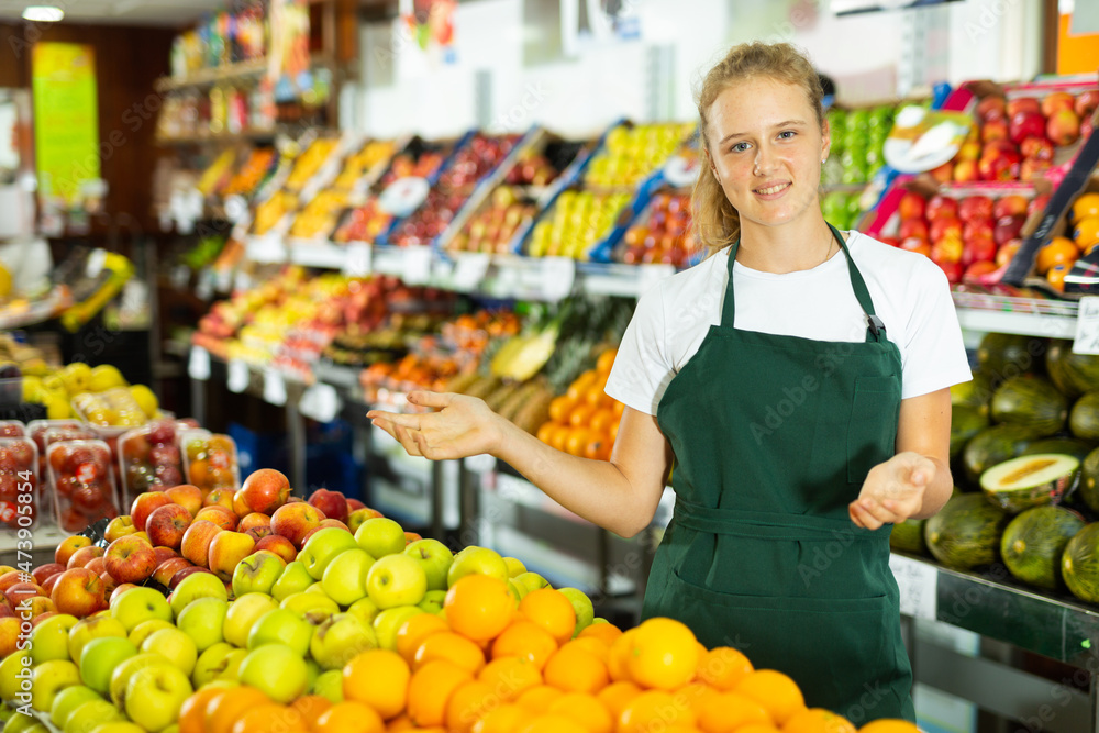 Portrait of teenage girl working in grocery shop as job experience, selling ripe oranges