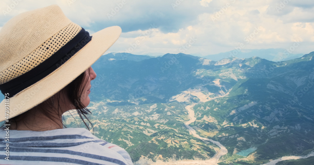 Fototapeta premium Close-up, woman traveler looking at mountains view from top. Happy woman traveler portrait in straw hat watching at scenery summer mountain landscape. Travel, trekking concept. Albania, Dajti