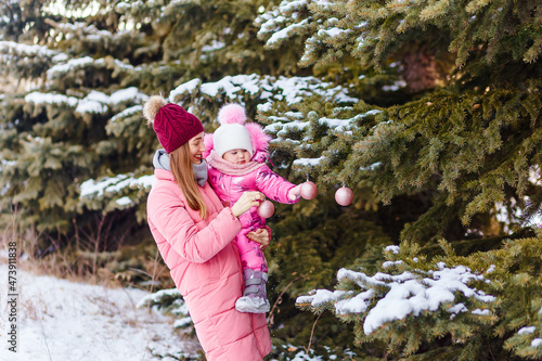 a young woman and a little girl hang balls on a eding tree in winter photo