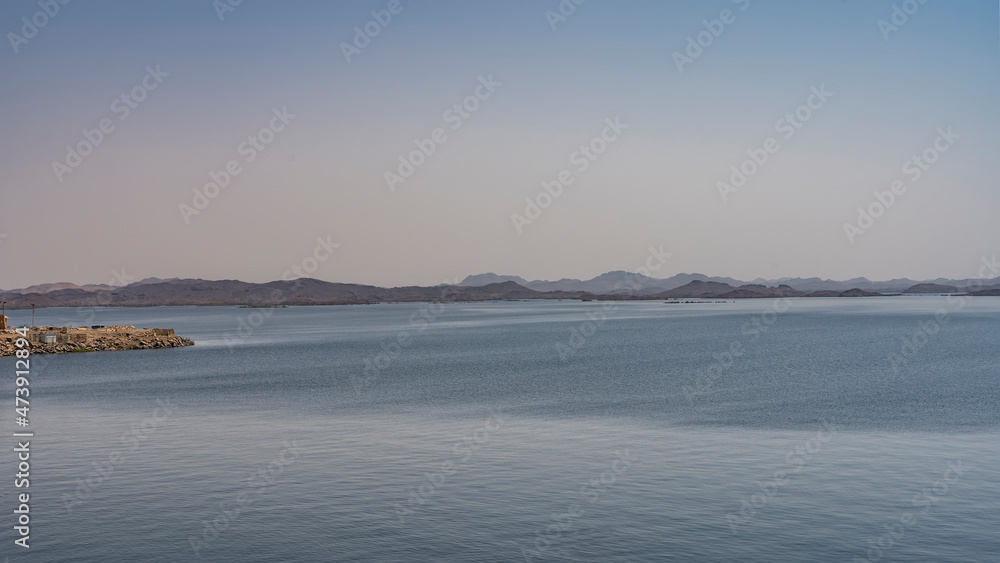Aswan reservoir in Egypt. Ripples are visible on the calm surface of the blue water. In the distance, against the background of the azure sky, a picturesque mountain range