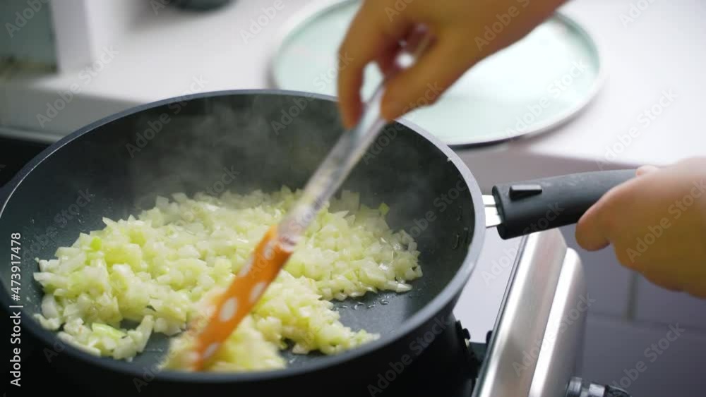 Frying chopped onions in preheated oil in black pan in the kitchen at home. Slices of chopped light onion are mixed with silicone spatula. Healthy eating, vegetables, cooking at home Frying chopped onions in preheated oil in black pan in the kitchen at home. Slices of chopped light onion are mixed with silicone spatula. Healthy eating, vegetables, cooking at home