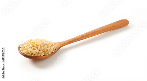 Brown rice in a wooden spoon placed on a white background.