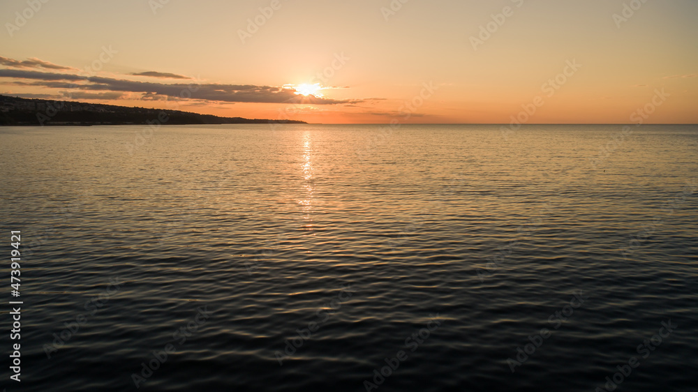 Sunrise over the sea. Calm sea with sunrise sky and sun through the clouds over. Tranquil seascape.