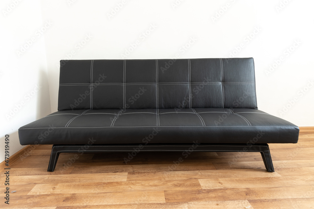 Modern black leather convertible sofa bed, wooden floor. Empty waiting