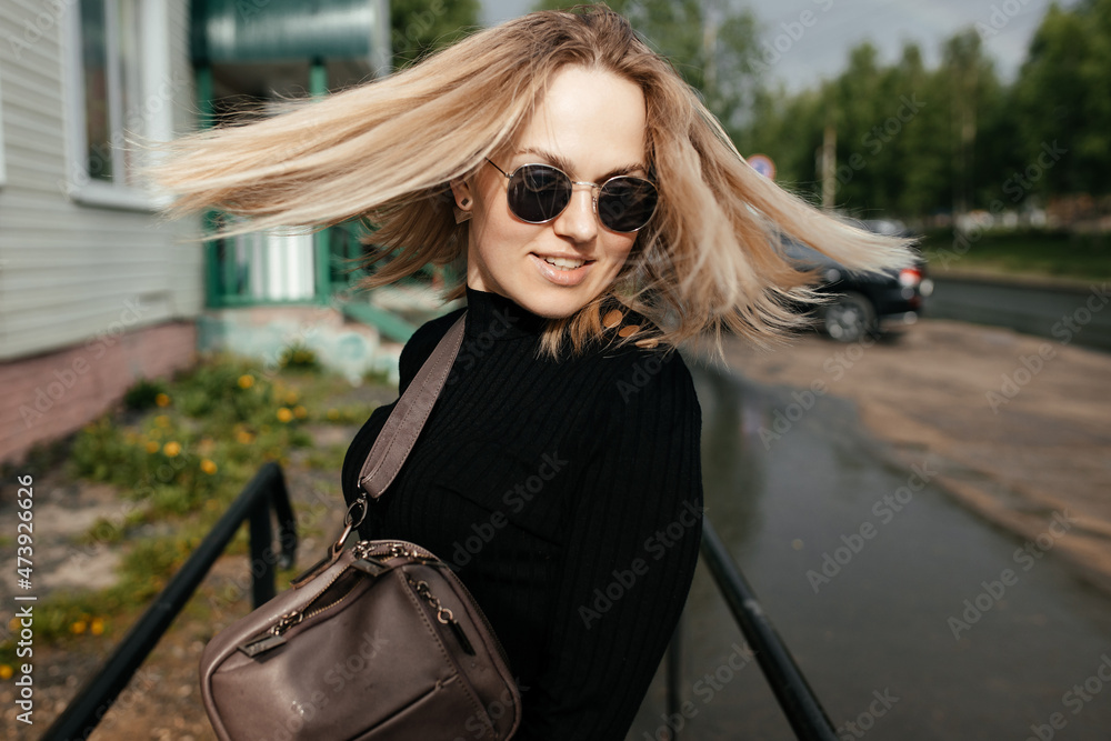 Close-up. a beautiful girl is enjoying a summer day in the city. Blonde in glasses with developing wet hair walks around the city.